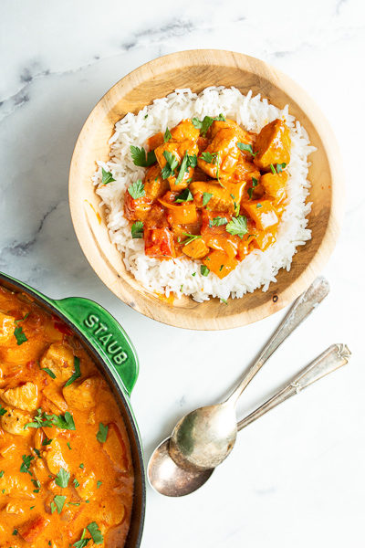 Overhead shot of chicken paprikash in bowl over rice with spoons